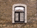 Visai savdabīga kompozīcija - brūns plastmasas pakešu logs, aiz tā ķieģeļu mūris. Mūkusalas 11, Rīga